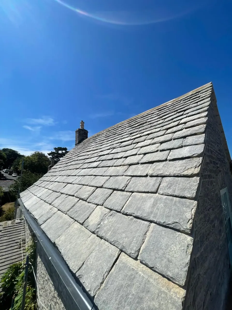 Completed Purbeck stone roof slope and stone gable beneath a clear blue sky