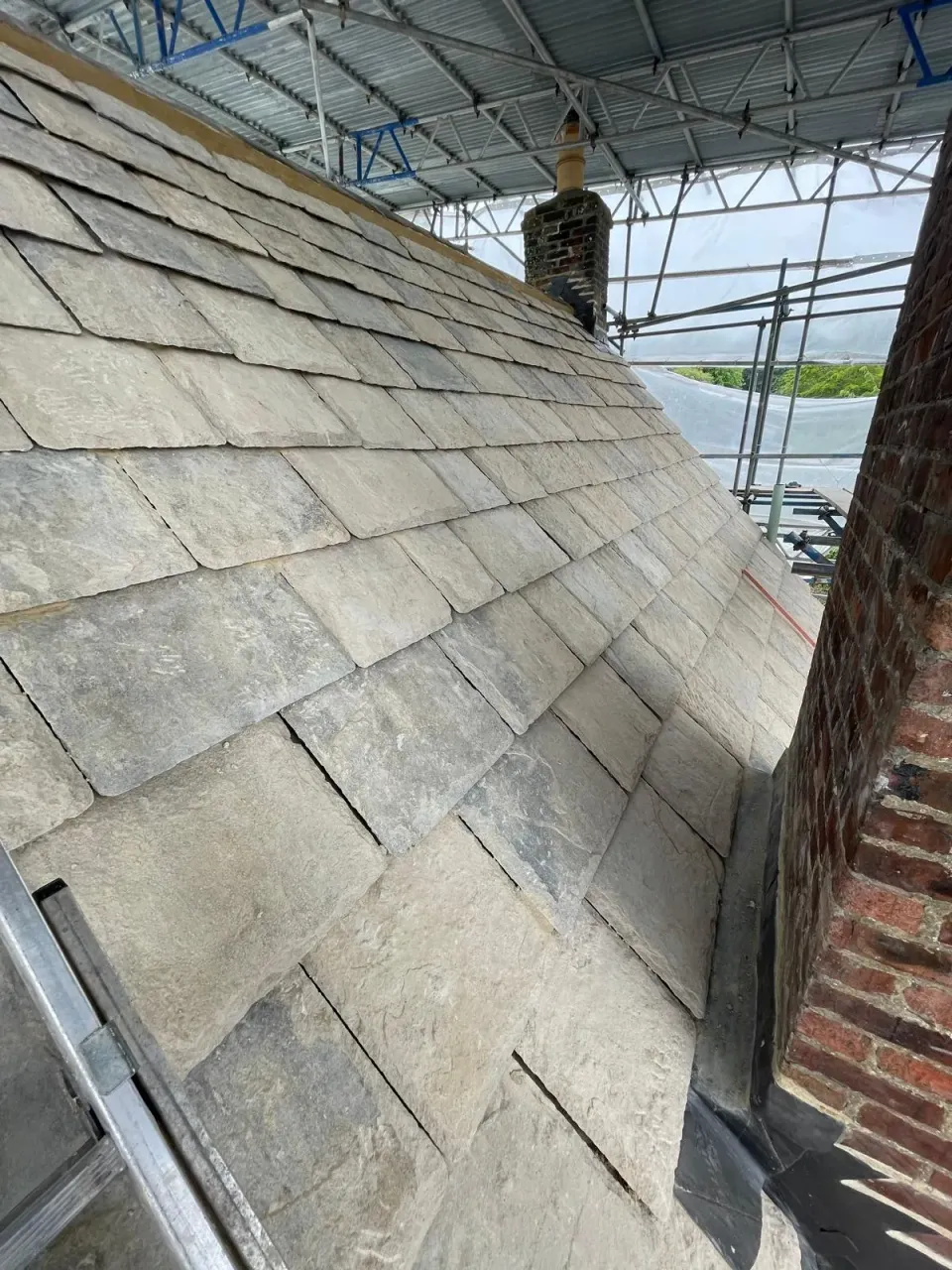 Purbeck stone roof courses meeting the lead flashing at a brick chimney under scaffolding