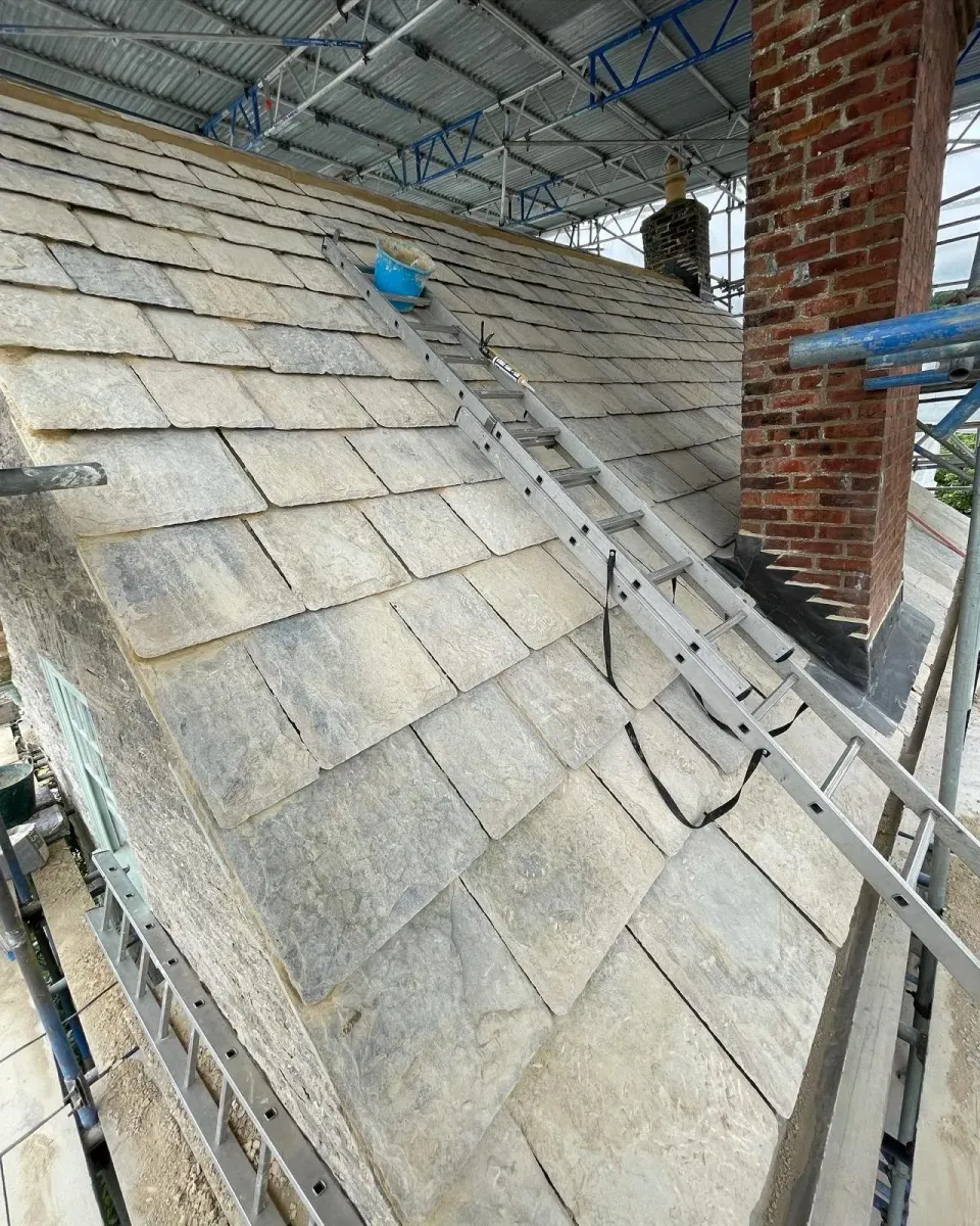 Individually fitted Purbeck roofing stones beneath temporary scaffold cover beside a brick chimney