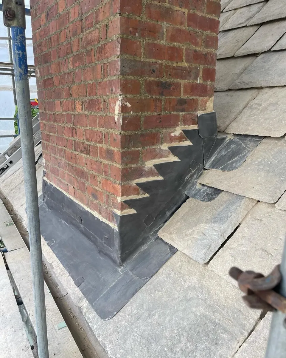 Close-up of stepped lead flashing around a brick chimney adjoining Purbeck roofing stones