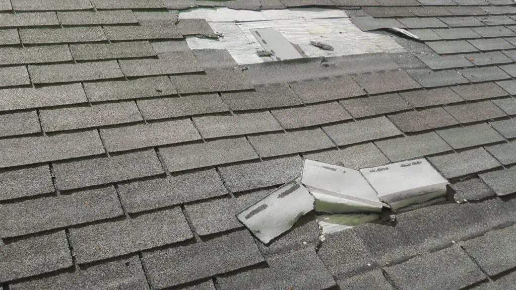 Storm-damaged pitched roof with missing and torn shingles requiring urgent roofing repairs.