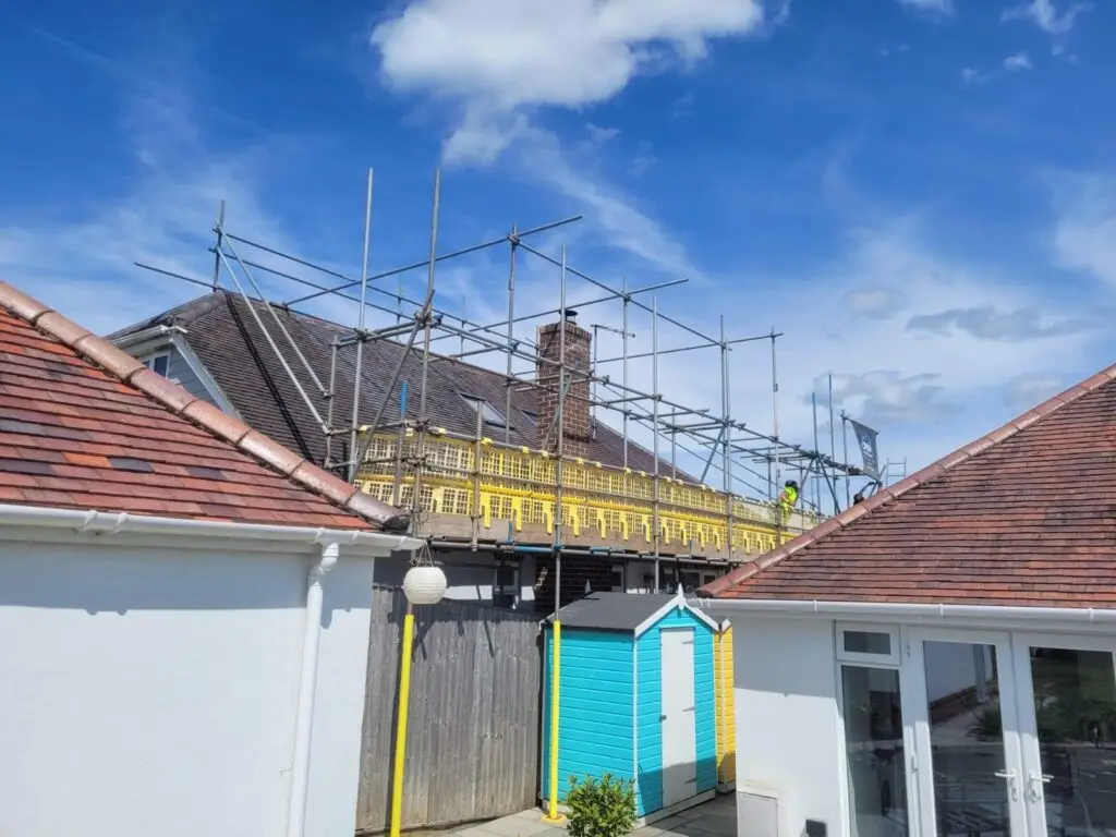 Rear view of a residential solar panel installation project in Dorset by Up Top Solar. Professional scaffolding by Up Top Scaffolding with qualified roofer working on pitched roof preparing for solar PV panel mounting and fitting.